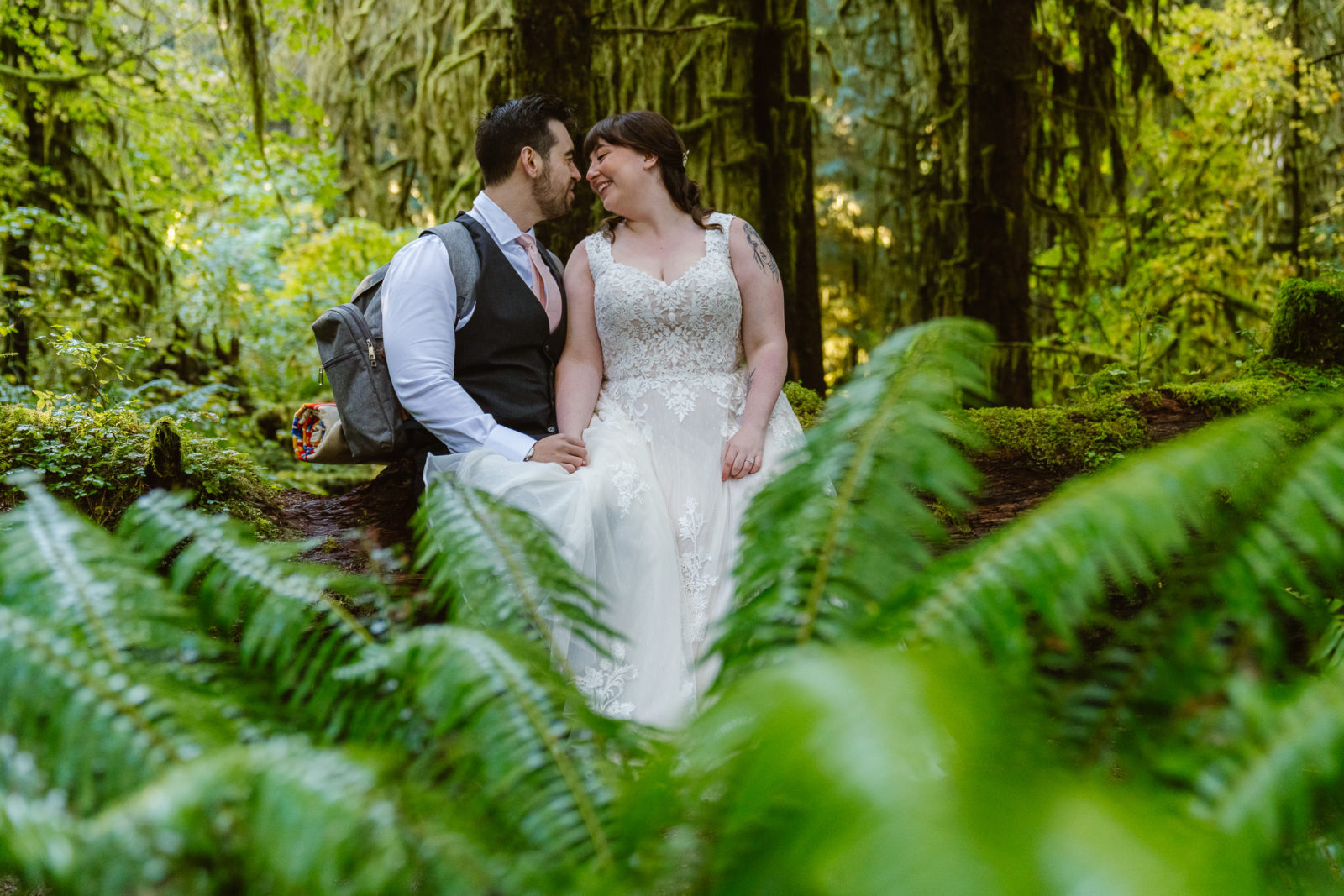 Couple sits on a log in the Hoh rainforest while hiking through on their elopement day in Olympic National Park